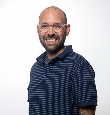Michael Johnson is a bald man with a beard, mustache, and glasses. He is wearing a dark blue striped polo shirt in front of a white background.