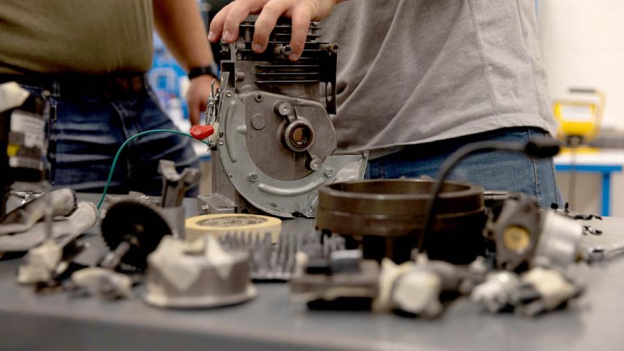 A close-up of students hands working on a small engine